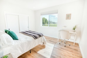 A bedroom with a bed, a desk, and a window with a view of greenery. - Edna Valley Modern Barndominium (Arroyo Grande)
