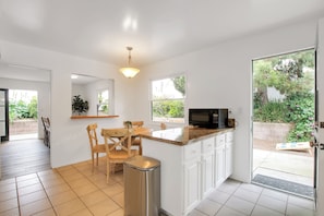 A modern kitchen with white cabinets, a granite countertop, and a dining area with wooden chairs.