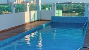 Ein Pool auf dem Dach mit einer Holzterrasse und Blick auf die Stadt.