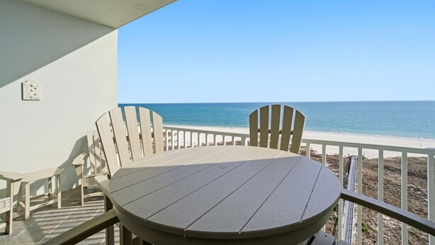 A balcony with a round table and chairs, overlooking a beach with the ocean in the background. - Tidewater 804 (Orange Beach)