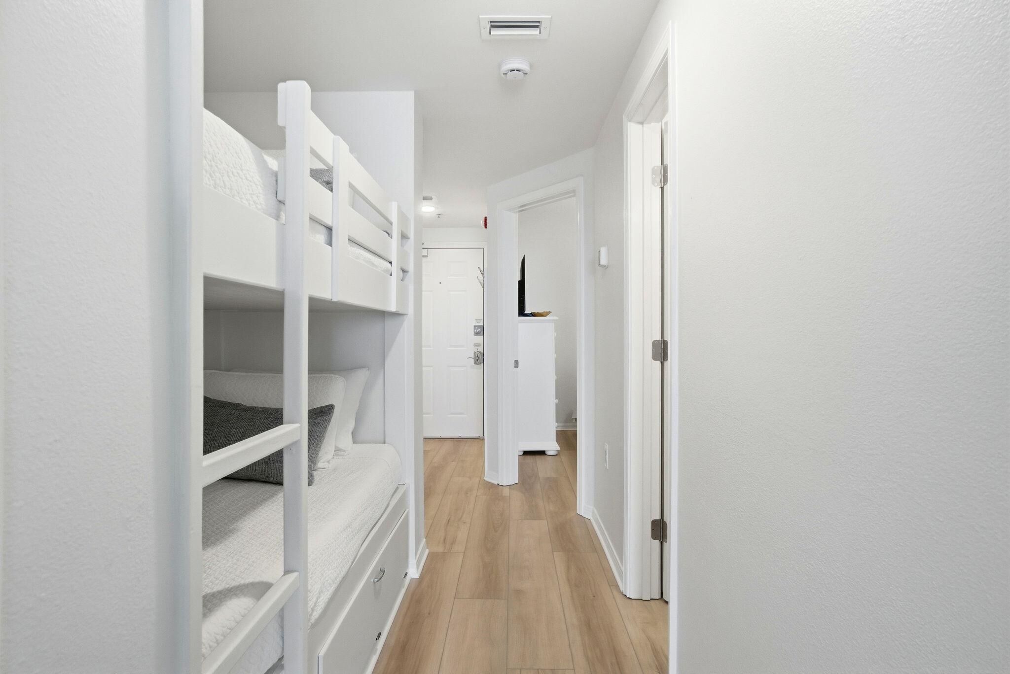 A narrow hallway with bunk beds on one side and a door leading to another room on the other.
