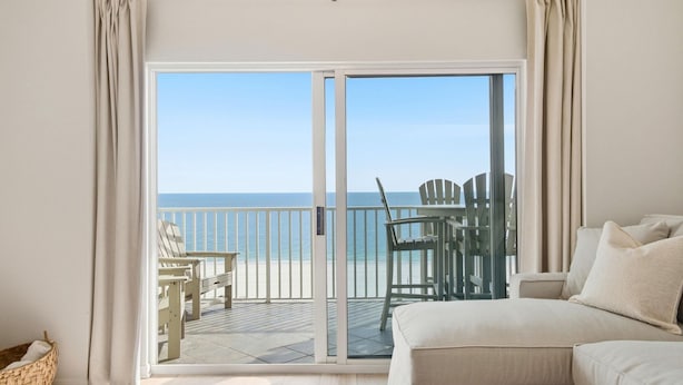 Ein Zimmer mit einer Schiebeglastür, die auf einen Balkon mit Liegestühlen und einem Tisch führt.
