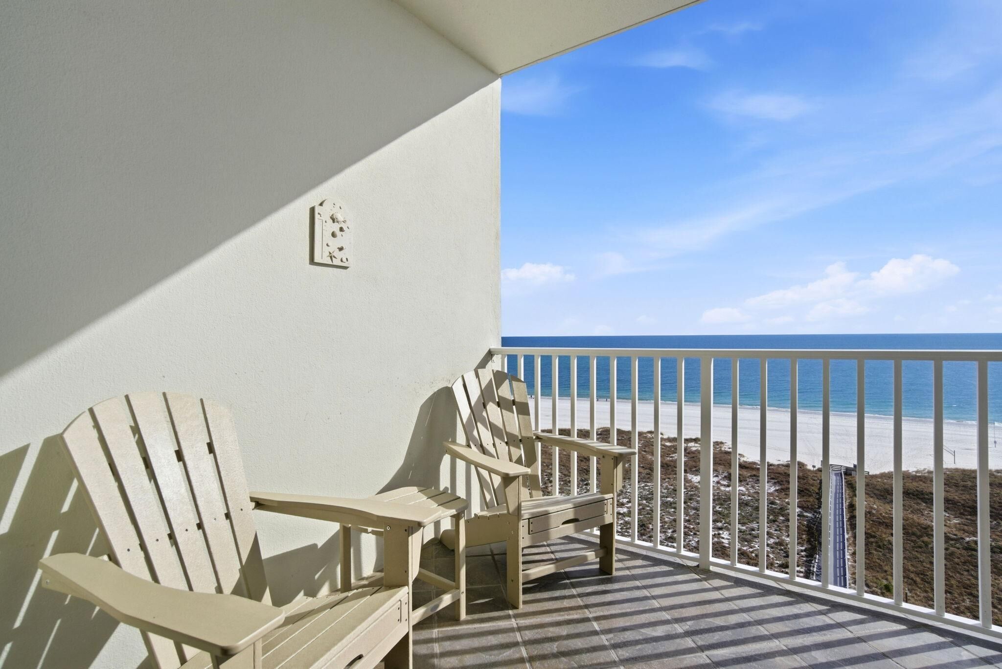 A balcony with two Adirondack chairs and a view of the beach.