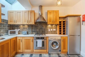 A modern kitchen with wooden cabinets, a stainless steel range hood, a microwave, a toaster, a stove, a washing machine, and a refrigerator. - Charming 2BDR Cottage by the Liffey and 3Arena (Dublin)