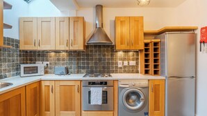 Eine moderne Küche mit Holzschränken, einer Edelstahl-Dunstabzugshaube, einer Mikrowelle, einem Toaster, einem Herd, einer Waschmaschine und einem Kühlschrank.