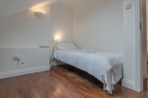 A small, single-bed room with a wooden floor, white walls, and a wall-mounted light fixture. - Charming 2BDR Cottage by the Liffey and 3Arena (Dublin)