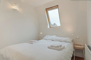 A bedroom with a single bed, a bedside table, a nightstand, a window, and a wall-mounted light fixture. - Charming 2BDR Cottage by the Liffey and 3Arena (Dublin)
