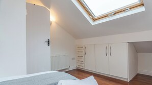 Ein Schlafzimmer mit Dachfenster, einem Bett mit grauer und weißer Decke, einem Heizkörper und einem Kleiderschrank mit mehreren Schubladen.