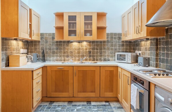 A modern kitchen with wooden cabinets, a tiled backsplash, and stainless steel appliances including a microwave, toaster, and stove. - Charming 2BDR Cottage by the Liffey and 3Arena (Dublin)