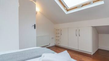 A bedroom with a skylight, a bed with a grey and white blanket, a radiator, and a wardrobe with multiple drawers.