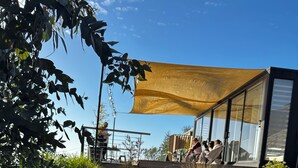 A modern building with a glass facade, a yellow canopy, and a landscaped area with mulch and rocks. - pro estancia 1 (constitución)