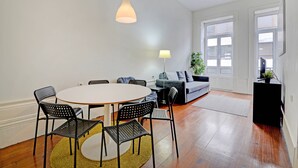 Ein modernes Wohnzimmer mit einem runden Esstisch, schwarzen Stühlen, einem grauen Sofa und einer Stehlampe.