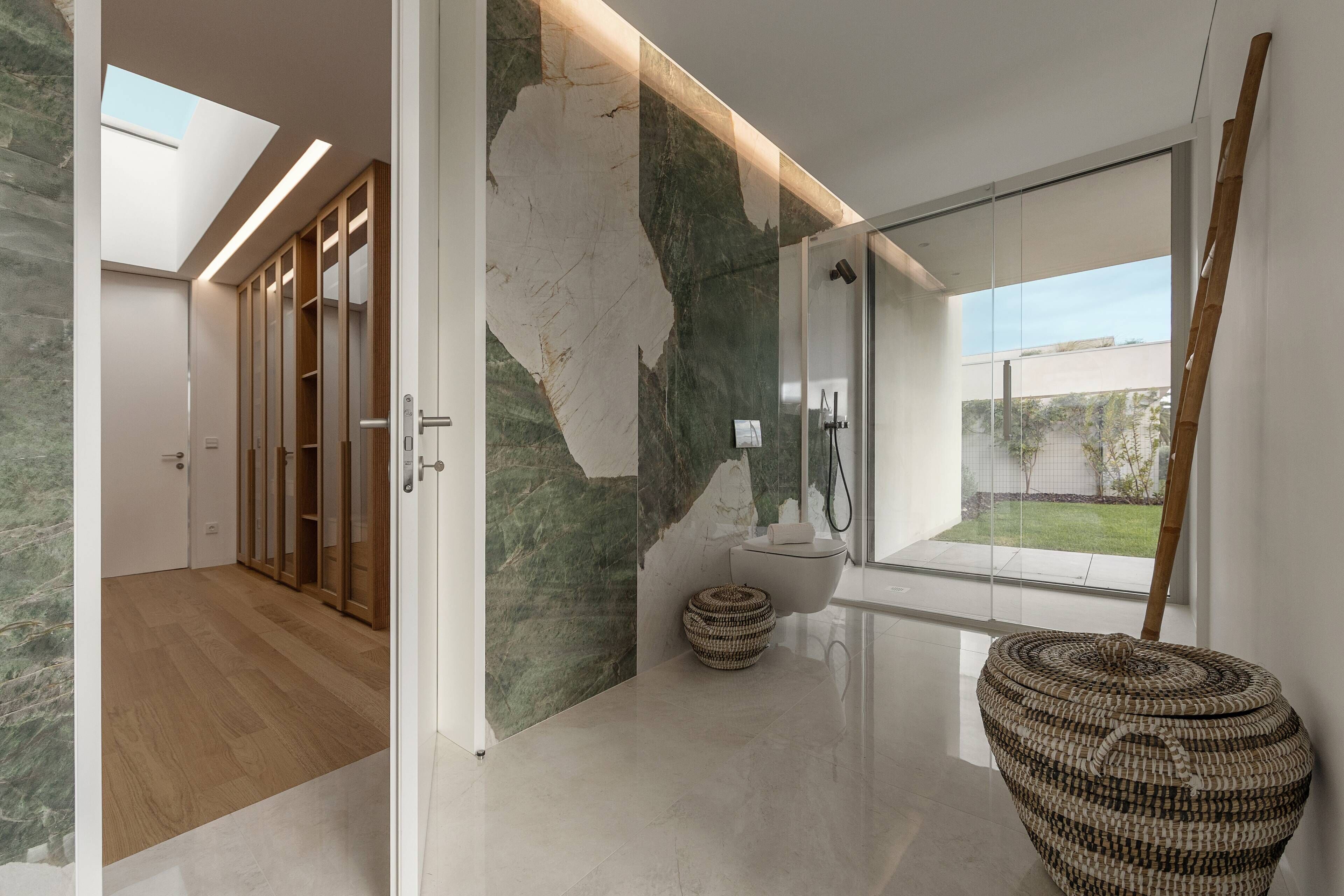A modern bathroom with a glass shower, a wooden door, and a large window.