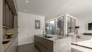A modern kitchen with a central island, a built-in oven, and a dining area with a table and chairs. - Lagoon Residence 56 Deluxe - Premium Accommodation (Óbidos)