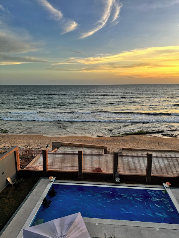 Une piscine avec vue sur la plage et l’océan au coucher du soleil.