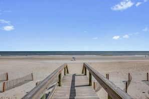 Ein hölzerner Steg führt zu einem Strand unter blauem Himmel.