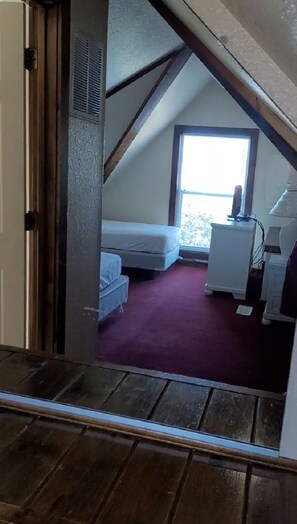 A bedroom with a sloped ceiling, a window, a bed, a small bedside table, and a desk with a lamp. - BIS-Duck - 2BR/2BA - Great Pools and Beach! (Duck)