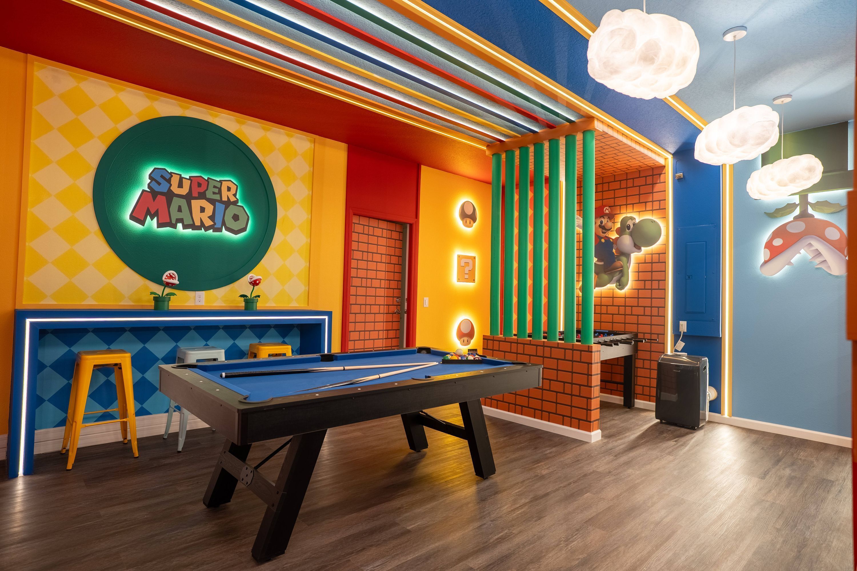 Una habitación vibrante con una mesa de billar, un letrero de Super Mario y un diseño de pared de ladrillo.