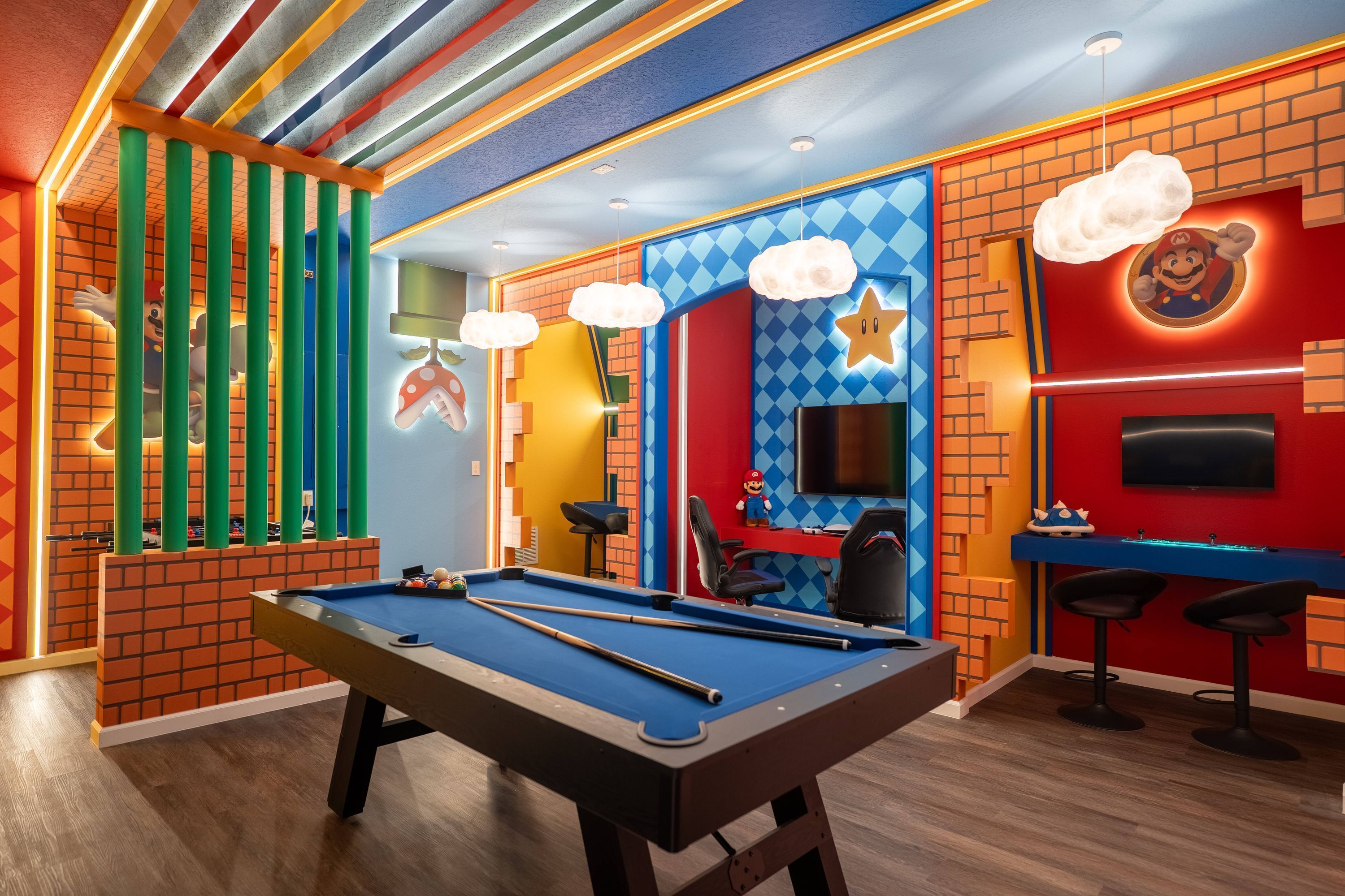 Ein Billardtisch in einem farbenfrohen Raum mit einer Nintendo-Wand, einem Fernseher und Barhocker.