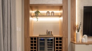 A modern kitchen with wooden cabinetry, a built-in wine cooler, and a countertop with glassware and a plant. - 7BR Windsor Cay w Game Room Pool Near Disney (Clermont)
