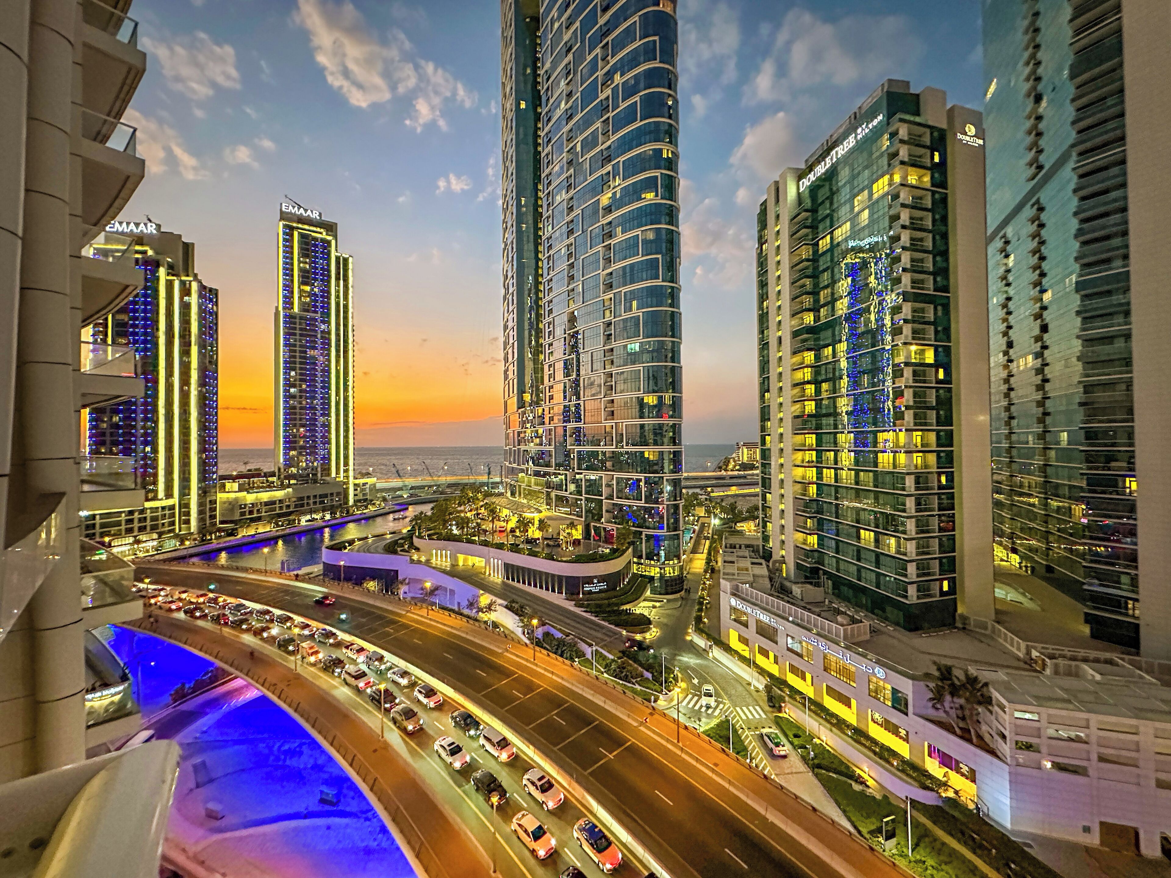 A cityscape with high-rise buildings, a busy road, and a body of water.