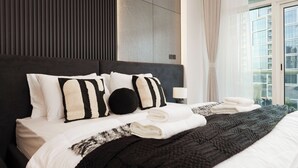 Ein modernes Hotelzimmer mit einem großen Bett, einer Kopfteil mit vertikalen Linien und Blick auf die Stadt durch große Fenster.