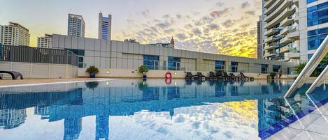 A swimming pool with a cityscape in the background, including modern buildings and a sunset.