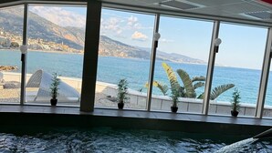 Une piscine intérieure offrant une vue sur un paysage côtier grâce à de grandes fenêtres.