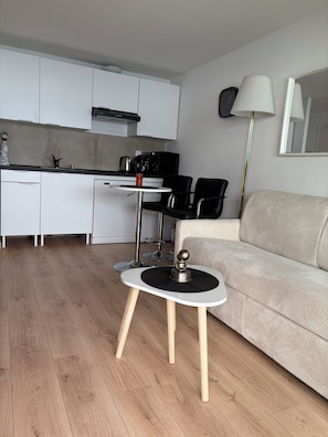 A modern kitchen with white cabinets, a black refrigerator, and a coffee machine. There is a round table with a decorative item on it, and a beige sofa in the living area. - Bellevue Palace , on the beach fully renovated&equipped apartment next to Monaco (Menton)