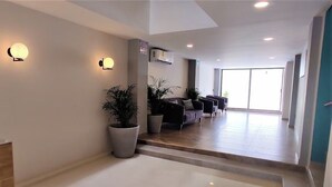 Een moderne hotel lobby met een receptiebalie, een zithoek en grote ramen.