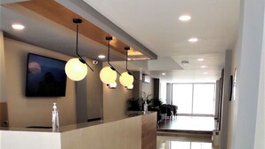 Een modern ingerichte receptie met een balie, een wandtelevisie, hanglampen en uitzicht over de lobby.