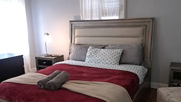 Un lit bien fait, avec une couverture rouge et deux oreillers, une table de chevet avec une lampe et un ventilateur de plafond.