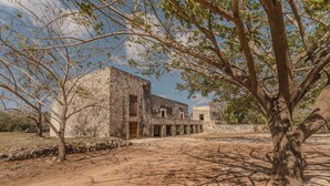 A courtyard with a stone building, a tree, and a clear sky. - Hacienda San José Xuilub (Espita)