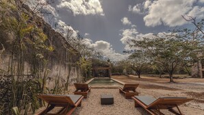 A pool area with wooden loungers and a small pool, surrounded by gravel and vegetation. - Hacienda San José Xuilub (Espita)