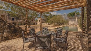 An outdoor seating area with a glass-top table and chairs, a pool, and a pergola structure. - Hacienda San José Xuilub (Espita)