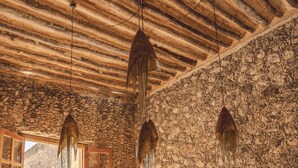 A rustic dining area with a large wooden table and chairs, stone walls, and hanging light fixtures. - Hacienda San José Xuilub (Espita)