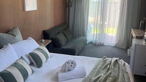 Una habitación de hotel con cama, escritorio, silla y ventana con cortinas.