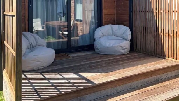 Una terraza moderna al aire libre con dos sillones de exterior blancos tipo bean bag, una valla de madera y un ventanal de vidrio que da a un patio.