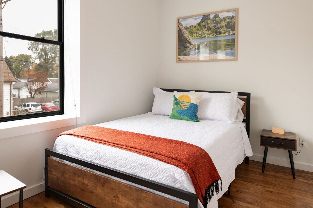 A bedroom with a bed, a nightstand, a window, and a painting on the wall.