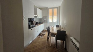 Una cocina compacta con electrodomésticos modernos, un comedor con mesa y sillas, y un ventanal que proporciona luz natural.