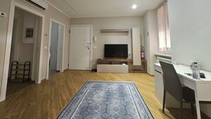 Una sala de estar moderna con un televisor de pantalla plana, un escritorio con una silla, un tapete estampado y piso de madera.