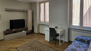 Una habitación con televisión, escritorio, silla, cama y ventanas amplias.