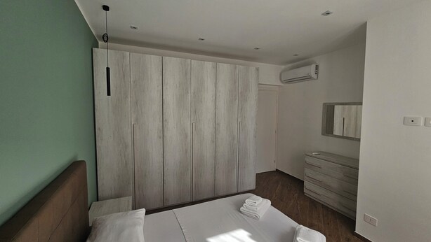 Un dormitorio moderno con dos camas, un armario de madera, un tocador con espejo y un equipo de aire acondicionado.