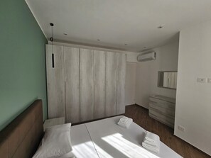 Et moderne soveværelse med to senge, et træskab, et sminkebord med spejl og en aircondition.