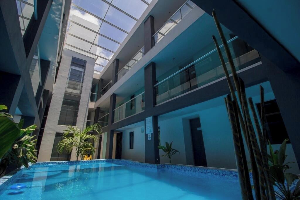 An indoor swimming pool with a glass ceiling, surrounded by modern architecture and indoor plants.