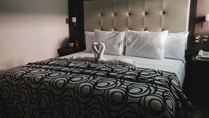 A hotel room with a tufted headboard, white bedding, and a patterned throw blanket.