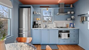 Cucina con pensili blu, frigorifero in acciaio inossidabile, piano cottura a gas e una finestra vista alberi.