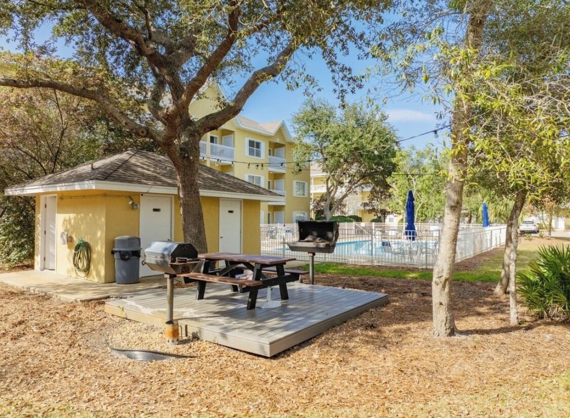 A yellow building with a covered patio, a barbecue grill, and a picnic table.