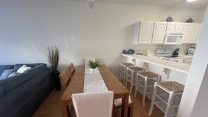 Une cuisine moderne avec des meubles blancs, un four à micro-ondes et une machine à café. On y trouve une table à manger avec des chaises et une plante en pot.