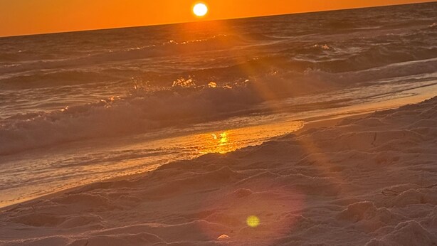Un coucher de soleil sur une plage, avec des vagues et un ciel dégagé.